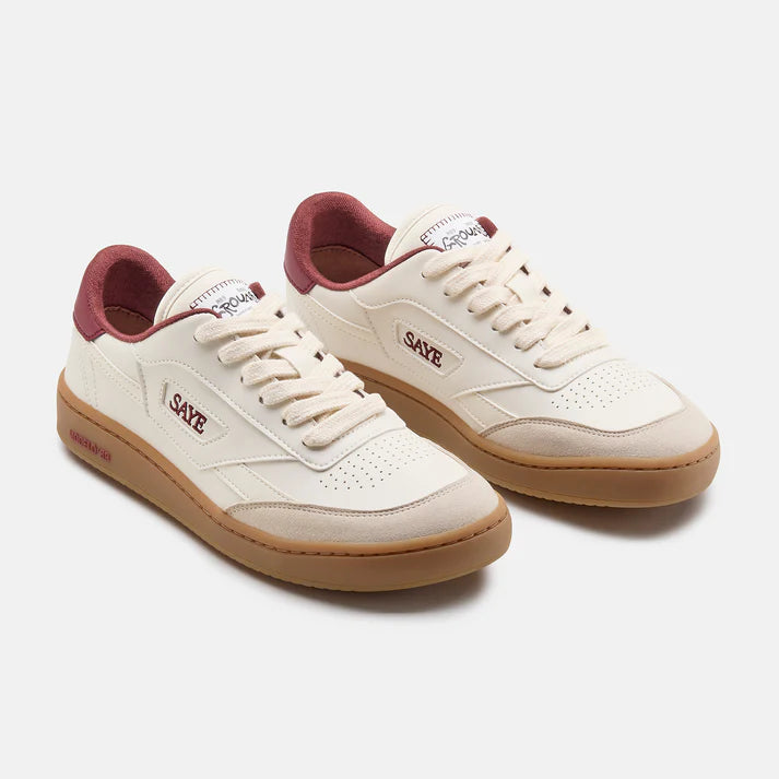 Weißer Sneaker von Saye mit bordeauxfarbenen Akzenten an der Ferse und hellbrauner Sohle, seitlich Markenname Saye in rot, Seitenansicht von vorne