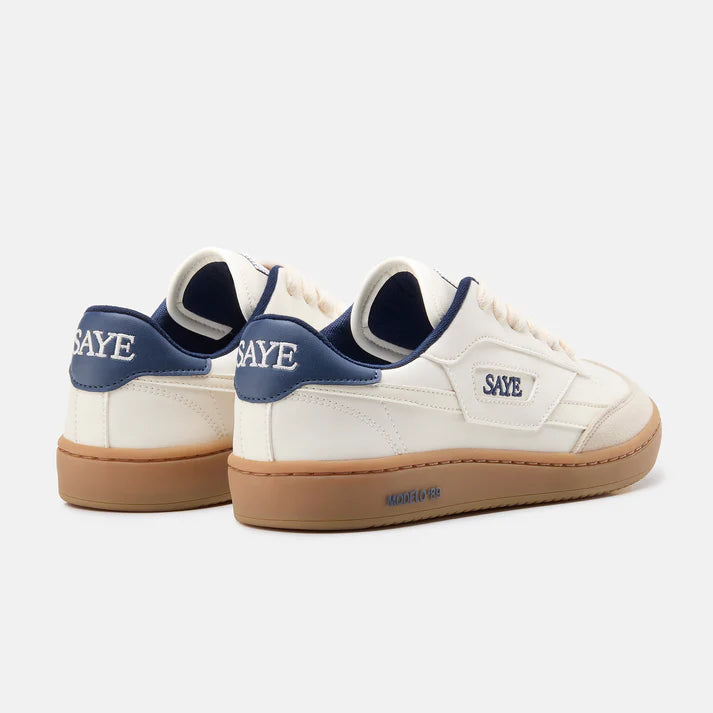 Weißer Barefoot Sneaker von Saye mit brauner Sohle und weißen Schnürsenkeln, an der Ferse mit blauen Akzenten, seitlich und hinten Markenname Saye in blau, Seitenansicht von hinten